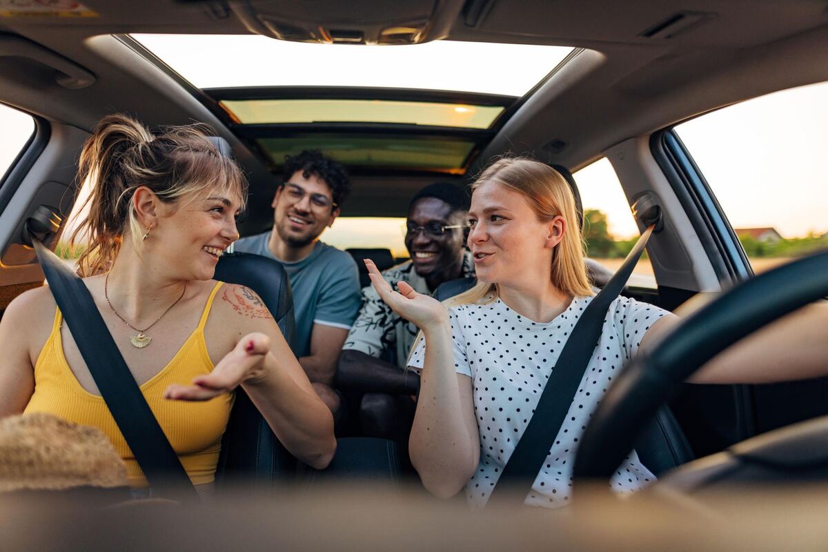 A driver talking with three passengers in the back seats of a moving car