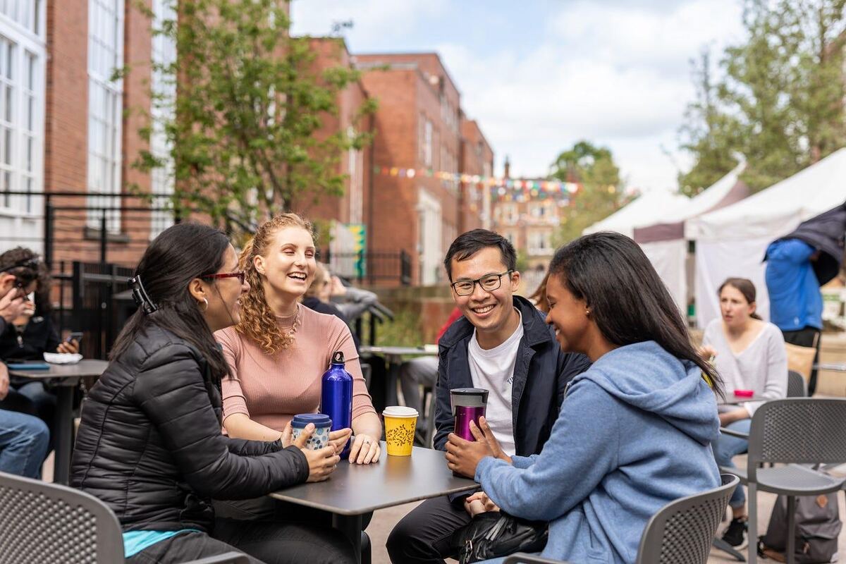 Students laughing over takeaway cups at an outdoor market table